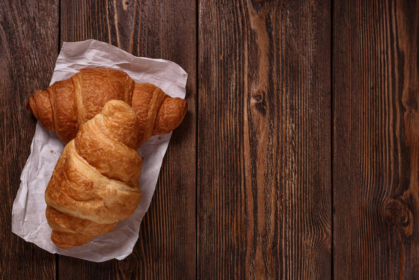 Freshly croissants on white paper on dark wooden table. Sweet and tasty dessert. Baking concept.Top view with empty place for text. - Photo, Image