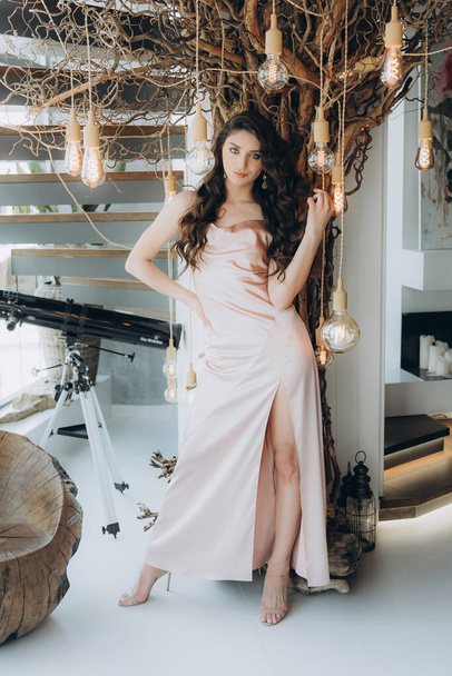 Beautiful, stylish, and elegant girl brunette, model, with makeup and curly hair in a peach-colored silk dress for a magazine photoshoot in fashion style. - Foto, immagini