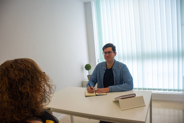 Eine Logopädin betreut eine Patientin in ihrer Praxis. Im Büro stehen ein weißer Tisch, eine Agenda und Schreibwaren. - Foto, Bild