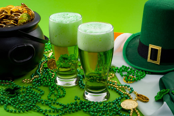 Удача ірландського мема і "Happy St Patricks day" концептуальна тема з двома склянками пофарбованого пива, капелюха лепрекона, намиста і горщика з золотими монетами на ірландському прапорі ізольовані на зеленому фоні - Фото, зображення