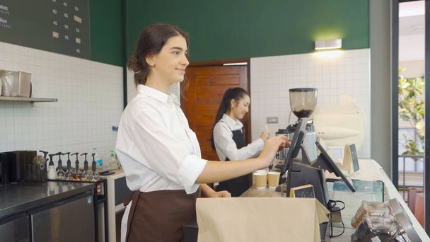Önlüklü Ortadoğu Kadını kahvecileri siparişleri topluyor, tezgahtaki müşterilerle konuşuyor, kafe kasiyeriyle görüşüyor. İş hizmeti. İnsan yaşam tarzı. - Fotoğraf, Görsel