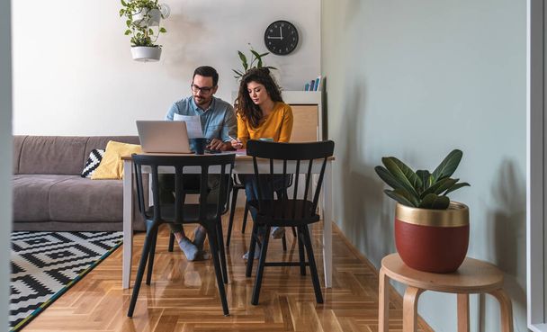 Couple manage finances together at home. Husband and wife holding household bills or taxes, calculating expenses together, sitting at desk and using computer - Foto, afbeelding