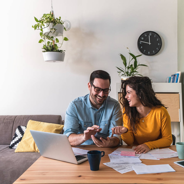 Ευτυχισμένοι σύζυγοι διαχειρίζονται οικονομικά μαζί στο σπίτι. Χαμογελώντας χαρούμενα παντρεμένο ζευγάρι υπολογισμού και πληρωμής λογαριασμών σε απευθείας σύνδεση στον υπολογιστή laptop στο σπίτι - Φωτογραφία, εικόνα