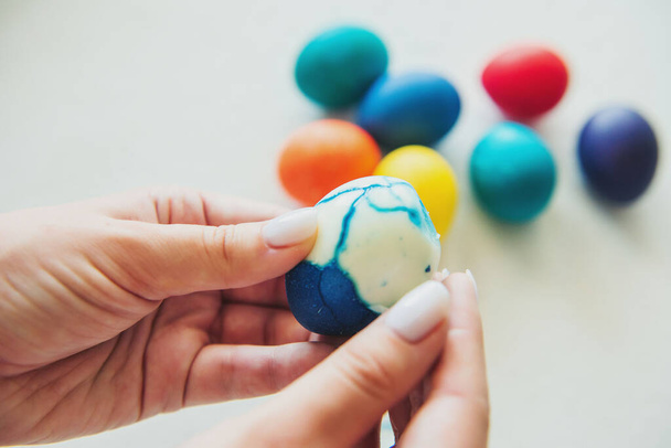 αυγά. Πάσχα. Πασχαλινά αυγά. χρωματιστά αυγά. Αυγά σε λευκό φόντο. Μελιτζάνα. Το κορίτσι καθαρίζει ένα αυγό. Γυναικεία χέρια - Φωτογραφία, εικόνα
