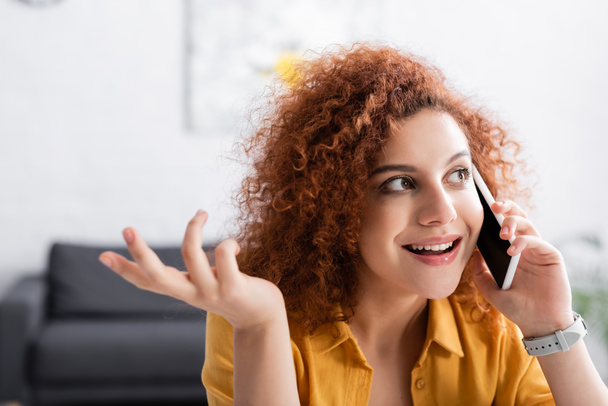 curly freelancer smiling and gesturing while talking on mobile phone - Photo, Image