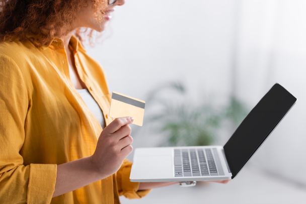 cropped view of woman holding credit card near laptop with blank screen - Foto, imagen