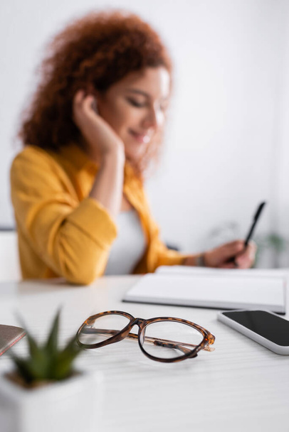 selective focus of eyeglasses and cellphone with blank screen near teleworker on blurred background - Fotografie, Obrázek