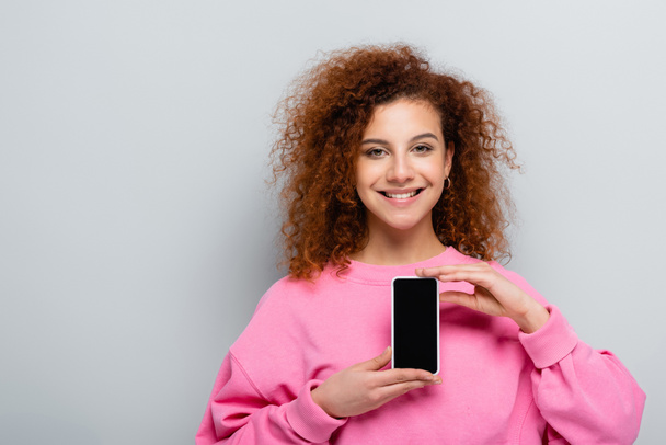 joyful woman showing smartphone with blank screen isolated on grey - Foto, Imagen