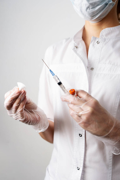 Closeup female doctor hands in gloves syringe with needle full of drug and disinfection cotton swab - 写真・画像