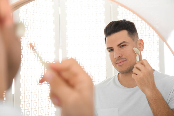 Man using mineral facial roller near mirror in bathroom - Foto, Imagen