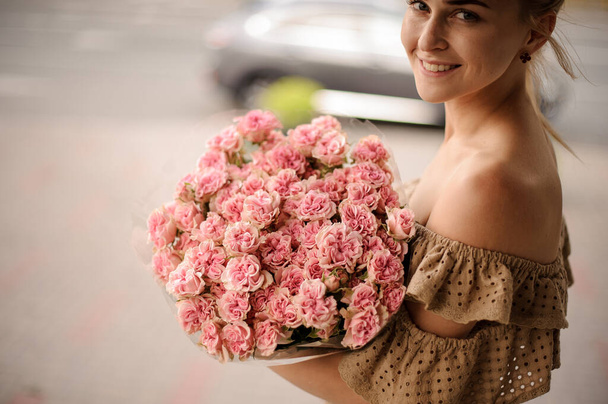 hermoso ramo de pequeñas rosas rosadas frescas en manos de una joven mujer sonriente - Foto, imagen