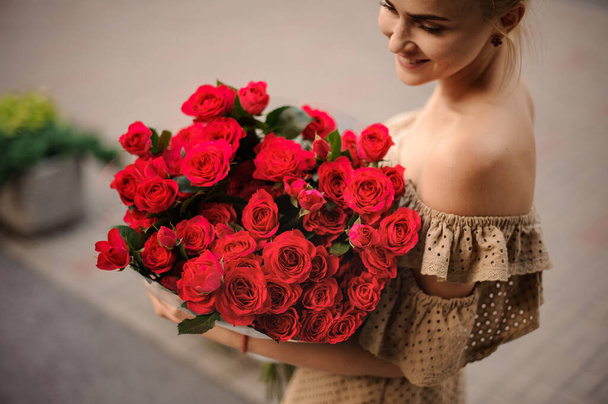 Great view of bright bouquet of red fresh roses in hands of young woman - Fotó, kép