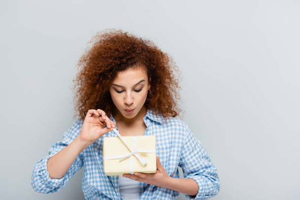mujer curiosa en camisa a cuadros apertura caja de regalo aislado en gris - Foto, Imagen