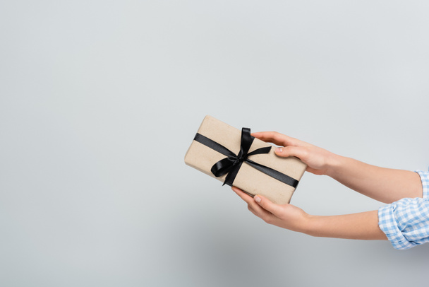 partial view of woman holding gift box with black ribbon on grey background - Fotoğraf, Görsel