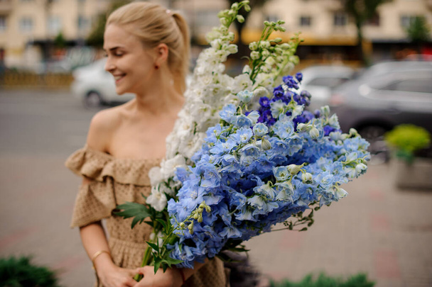 view on smiling blonde woman with bunch of multicolored delphinium flowers - Photo, Image