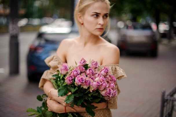 young blonde woman gently holding bouquet of beautiful purple roses in her hands - Фото, зображення