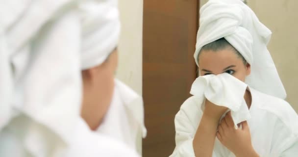 Kobieta delikatnie wyciera twarz miękkim ręcznikiem w pobliżu dużego lustra - Materiał filmowy, wideo