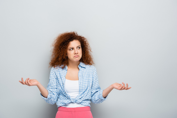 confused woman showing shrug gesture while looking away on grey background - Photo, image