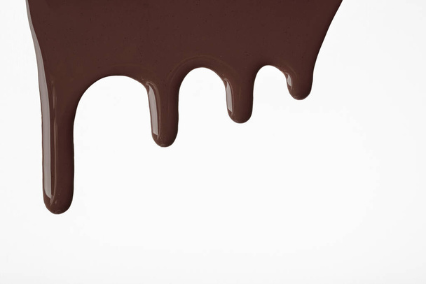 Gotas líquidas de chocolate oscuro de pintura fluyen hacia abajo sobre un fondo blanco aislado. Fondo de color marrón abstracto con patrón de goteo fluido. Pintura acrílica con espacio de copia. - Foto, Imagen