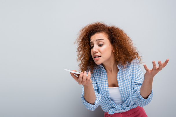 mujer irritada gesto al enviar mensaje de voz en el teléfono celular en fondo gris - Foto, imagen