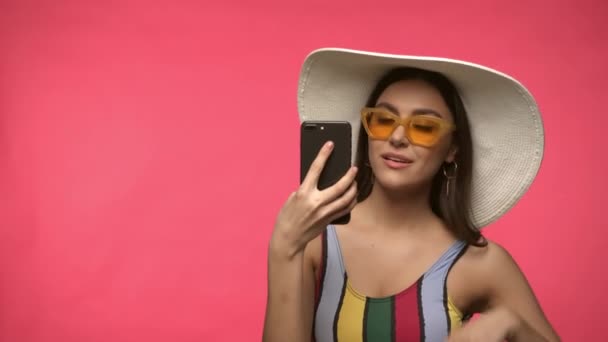 Kobieta w okularach przeciwsłonecznych i kapeluszu robi selfie na różowo - Materiał filmowy, wideo