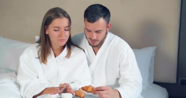 Krásný pár jí croissanty se snídaní na velké posteli - Záběry, video