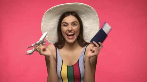 Woman in sun hat holding toy plane and air ticket isolated on pink - Footage, Video