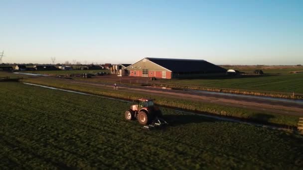 Traktor na farmě na travnatém pozemku při západu slunce letecké drone filmové záběry. - Záběry, video