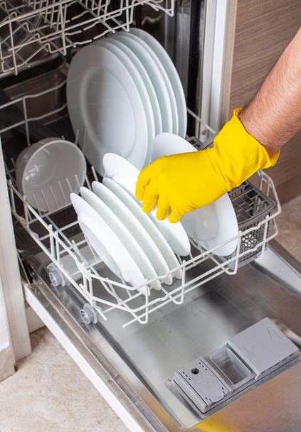 Detailní záběr mužských rukou s rukavicemi nakládající myčku nádobí s bílými talíři - Fotografie, Obrázek