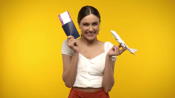 Mujer con pasaporte, billete de avión y avión de juguete aislado en amarillo - Imágenes, Vídeo