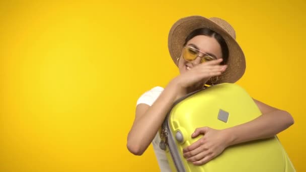 Χαμογελαστός ταξιδιώτης αγκαλιάζει βαλίτσα απομονωμένη στο κίτρινο - Πλάνα, βίντεο