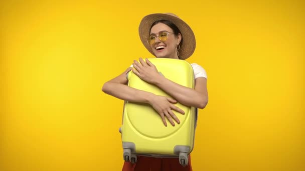 Šťastný cestovatel ve slunečních brýlích drží kufr izolovaný na žluté - Záběry, video