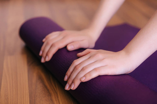 Weibliche Hände rollen blaue Gymnastikmatte auf den Boden, nachdem sie ihre Trainingseinheit im Yoga-Studio-Club oder zu Hause beendet haben. - Foto, Bild