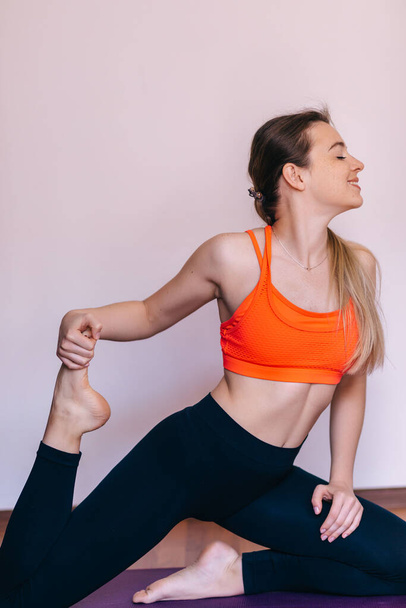 Skinny belle femme de yoga en leggings et haut de sport rose pratique yoga king pigeon pose sur tapis de yoga fitness, sport, personnes et mode de vie sain concept. - Photo, image