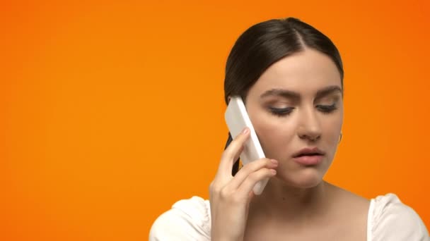 spięta kobieta rozmawiająca przez telefon komórkowy odizolowana na pomarańczowo  - Materiał filmowy, wideo