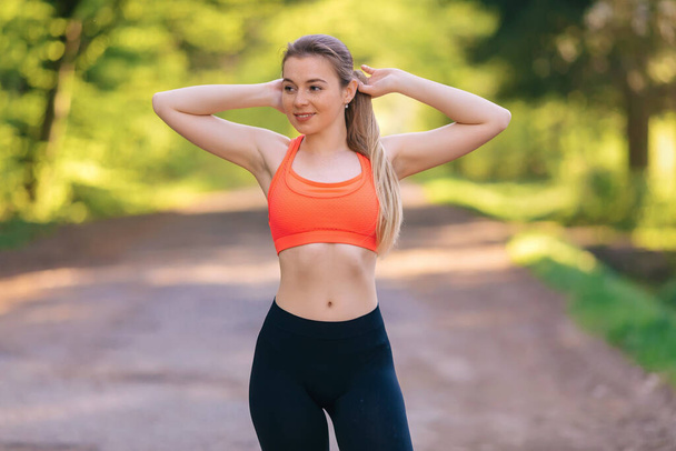 Beautiful young woman with long hair doing sport outdoor. Attractive female spending active time in the park. - Photo, Image
