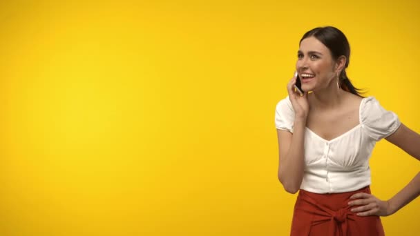 Smiling woman talking on smartphone and walking isolated on yellow - Footage, Video