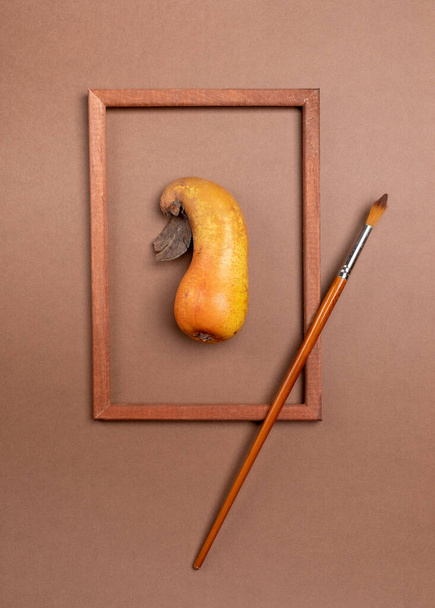 Wooden frame with ugly ripe pear inside it and brush on brown background. - Foto, Imagem