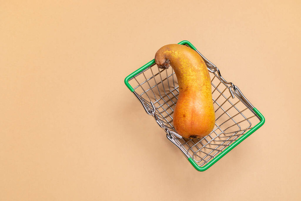 Pequeña cesta de la compra verde decorativa del supermercado con pera curva fea sobre fondo beige. - Foto, imagen