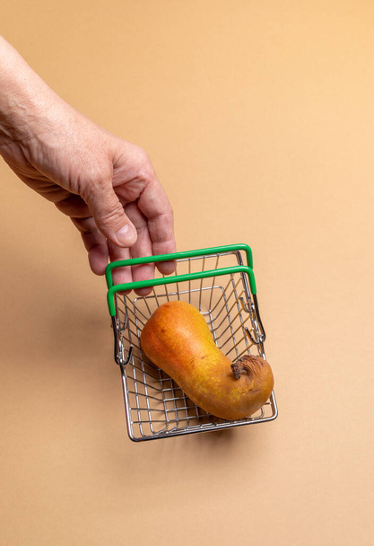 Main de femme atteignant pour la poire laide dans le petit panier de supermarché sur fond beige. - Photo, image