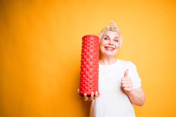 Joyful adult woman in white t-shirt holds fascia in hand and raises thumb up smiling broadly - Photo, Image