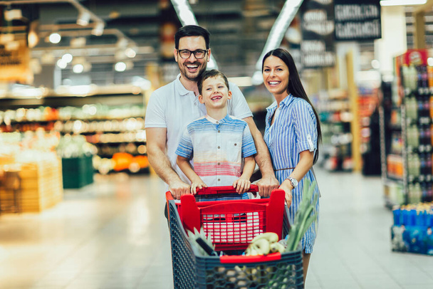 Happy family with child and shopping cart buying food at grocery store or supermarket - Foto, Imagem