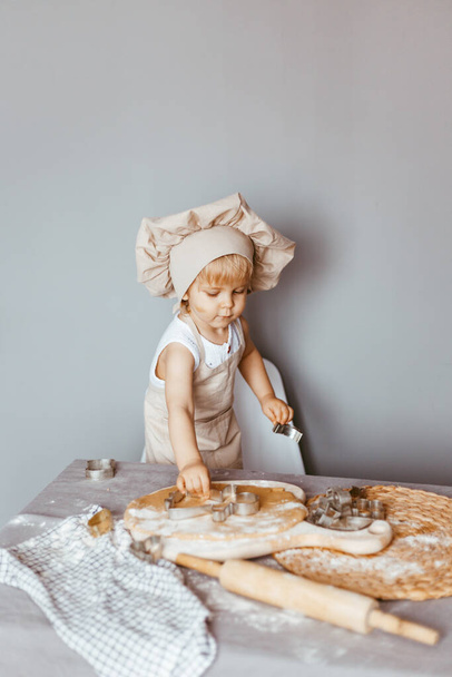 Cute boy prepares dough in the kitchen at home in an apron and a chef's hat - Φωτογραφία, εικόνα