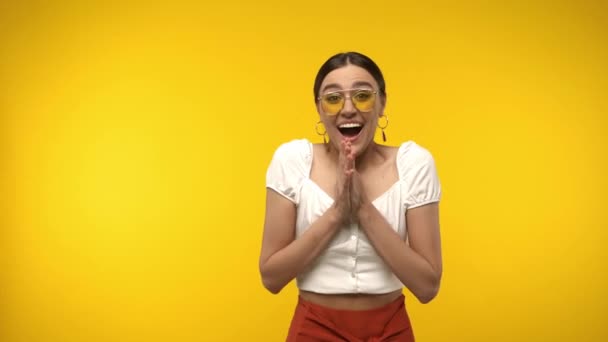 Mujer alegre en gafas de sol aplaudiendo aislado en amarillo - Metraje, vídeo