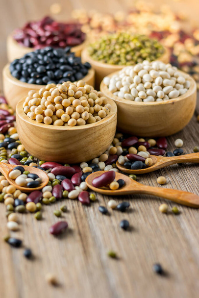 Various grains such as soybeans, black beans, red beans, dried corn in a wooden cup on a wooden table background. - Foto, Imagem