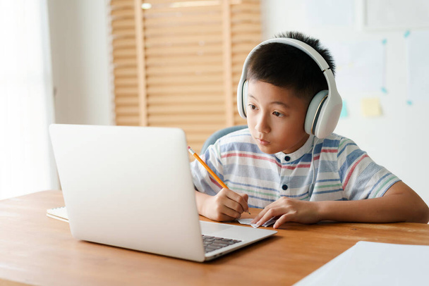 Asian little boy video call online via the internet tutor on a computer laptop with headphone. Asia man doing homework. Concept online learning at home  - 写真・画像