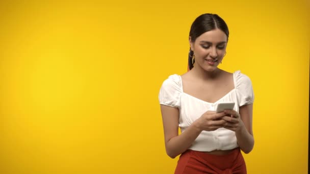 Lächelnde Frau mit Handy isoliert auf gelb - Filmmaterial, Video