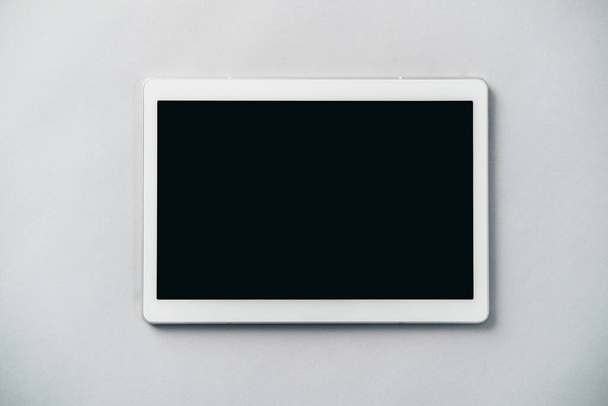 Close-up foto van witte digitale tablet met zwart scherm op grijze achtergrond, tafel bovenaanzicht, flat lay met kopieerruimte - Foto, afbeelding