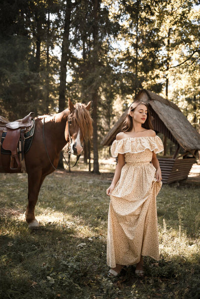 Una bella ragazza vestita con un vestito si trova vicino a un cavallo nella foresta - Foto, immagini