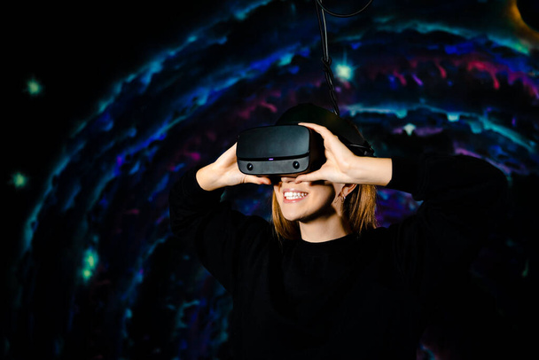 Smiling caucasian woman wearing vr glasses on the background of space, the girl smiling happily and enthusiastically while playing a virtual game. High quality photo - Foto, Imagen